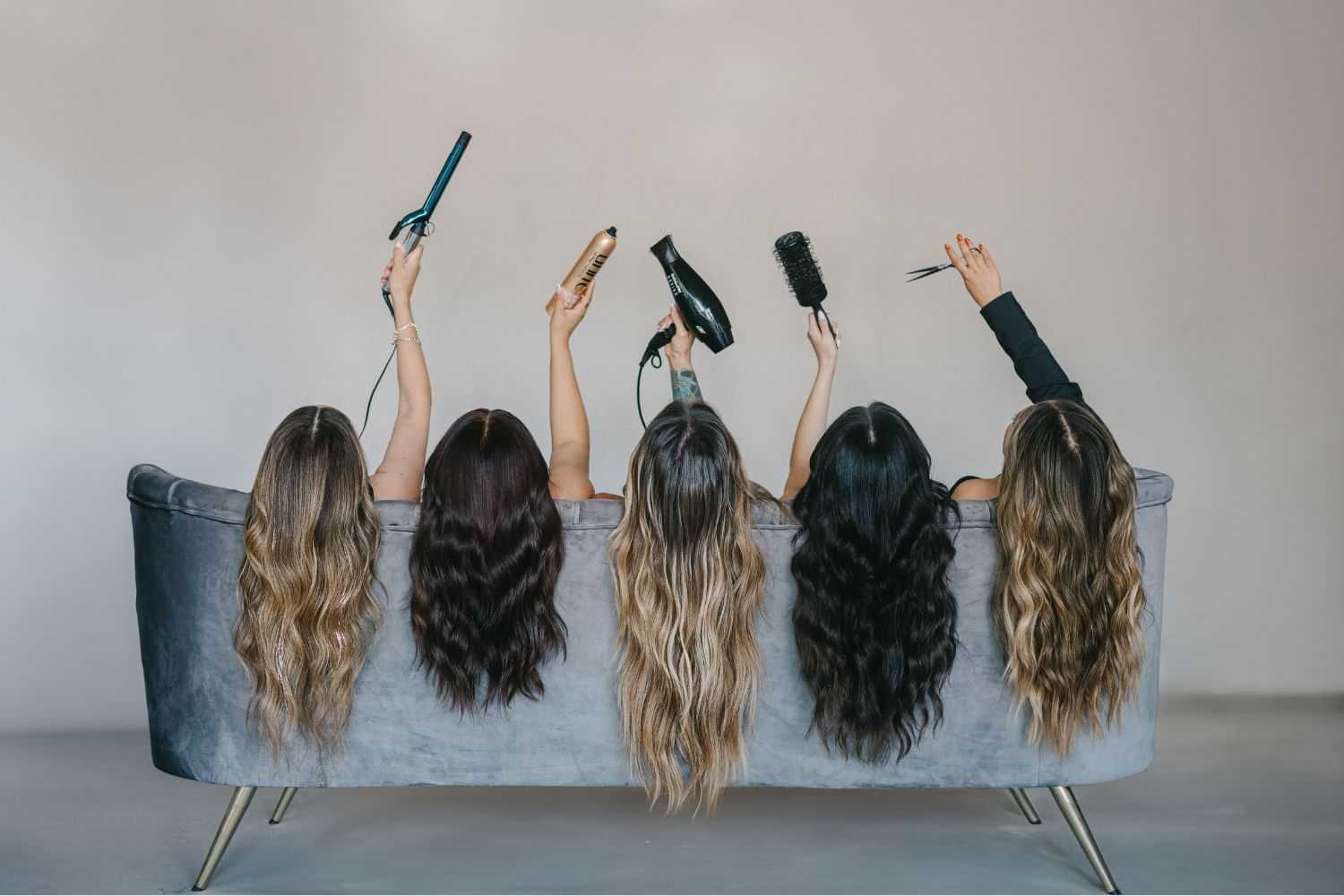 Five women showing styling tools behind a couch, showcasing diverse long hairstyles.